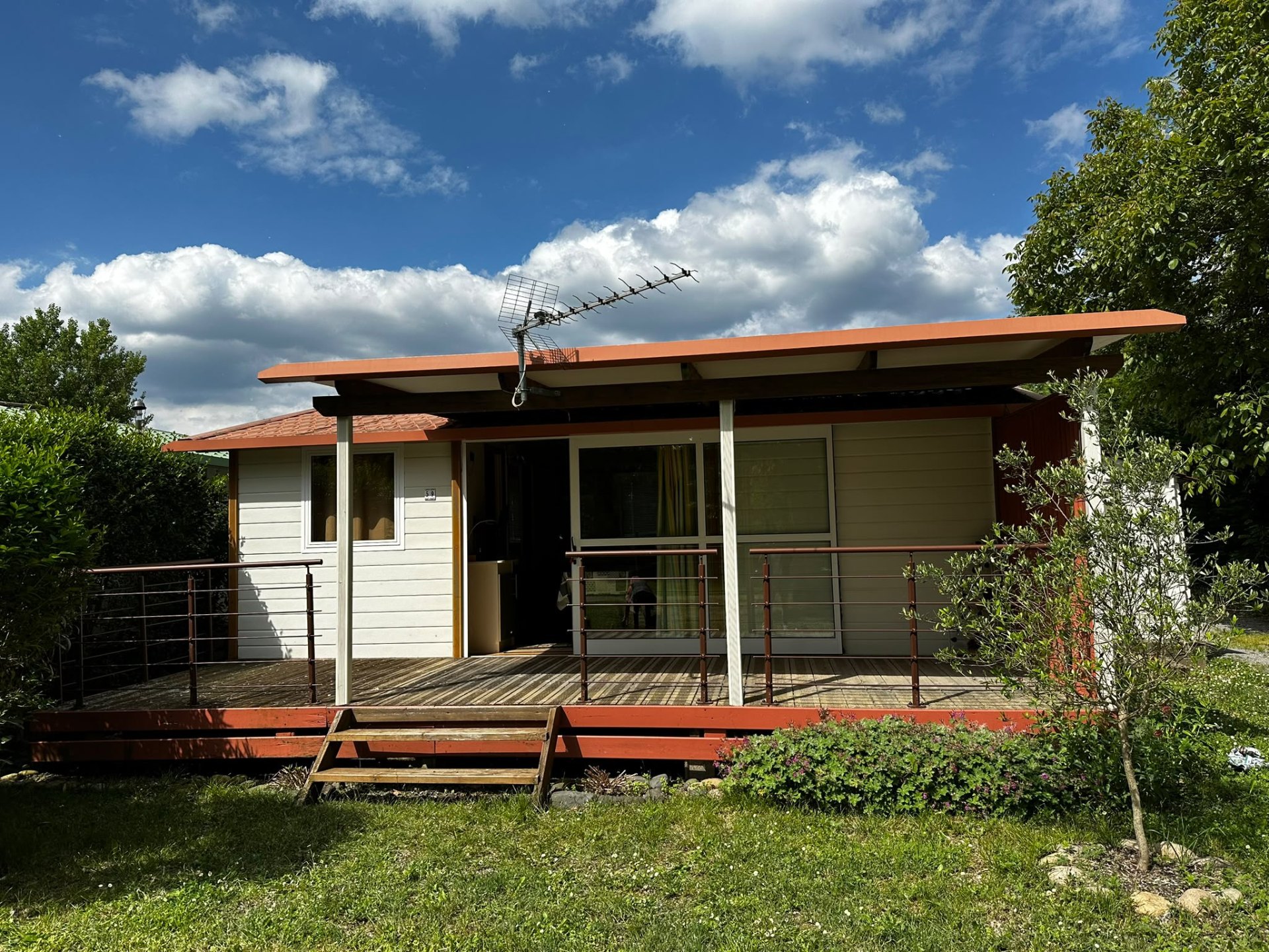 Chalet avec grande terrasse couverte en bois, entouré de verdure